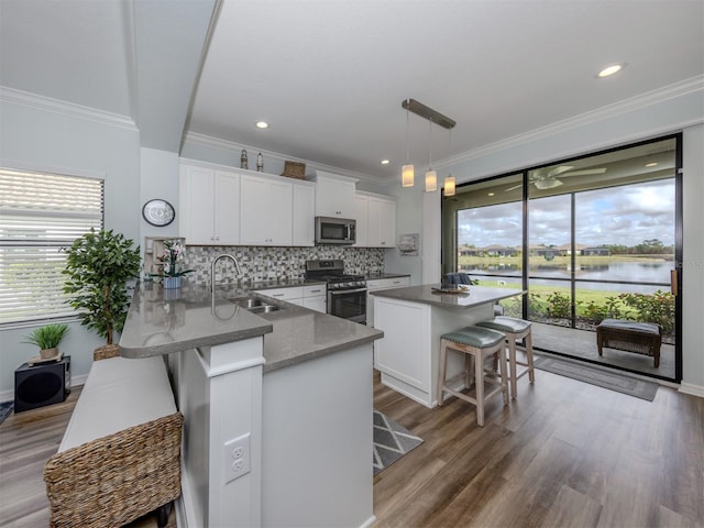 kitchen featuring a water view, sink, appliances with stainless steel finishes, a kitchen bar, and white cabinetry