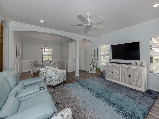 living room featuring hardwood / wood-style flooring, ceiling fan with notable chandelier, a healthy amount of sunlight, and ornamental molding