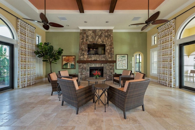 living room with beam ceiling, a stone fireplace, ceiling fan, and a high ceiling