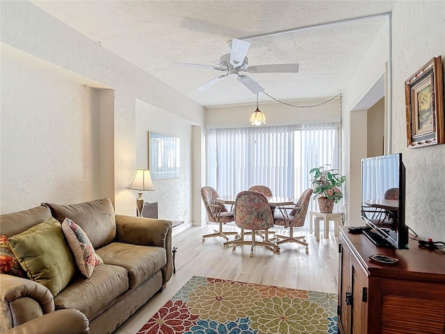 living room featuring light hardwood / wood-style floors, ceiling fan, and a textured ceiling