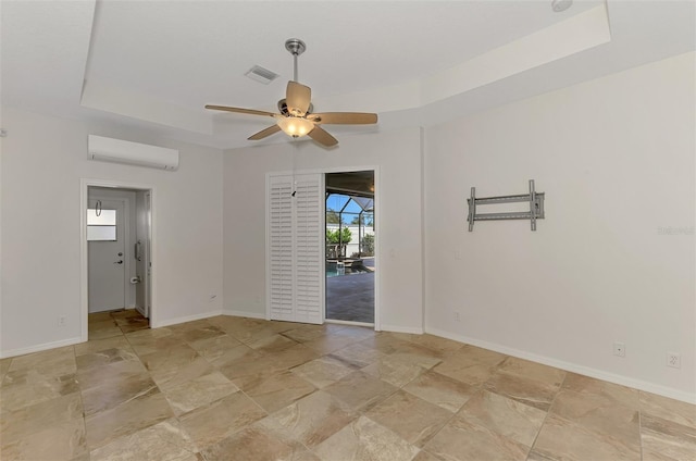 1219 Nantucket Rd, Venice, FL 34293 - empty room featuring a wall unit AC, a tray ceiling, ceiling fan, light stone finish flooring, and baseboards