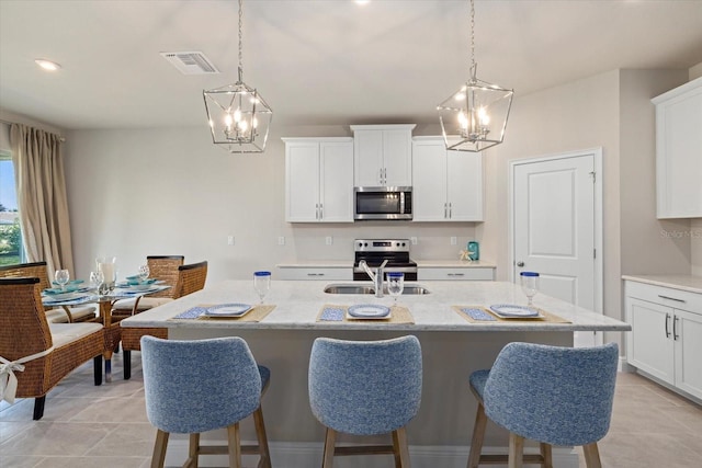 kitchen with a center island with sink, decorative light fixtures, white cabinets, and stainless steel appliances