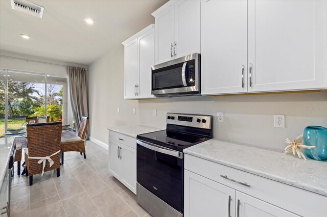 kitchen with light tile patterned flooring, stainless steel appliances, white cabinetry, and light stone counters