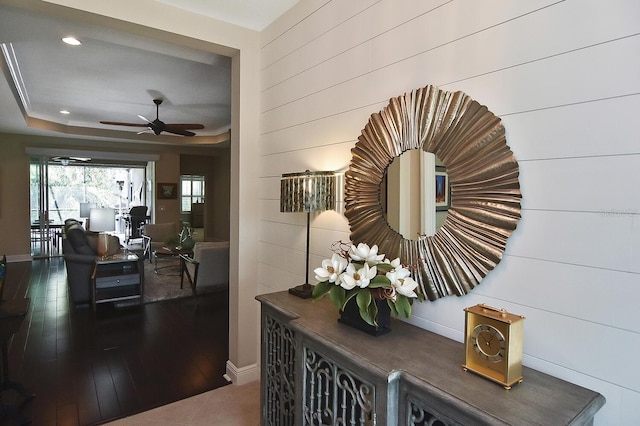 hall with wooden walls, hardwood / wood-style flooring, and a tray ceiling