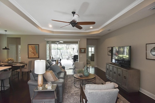 living room featuring dark hardwood / wood-style flooring, ceiling fan, a tray ceiling, and ornamental molding