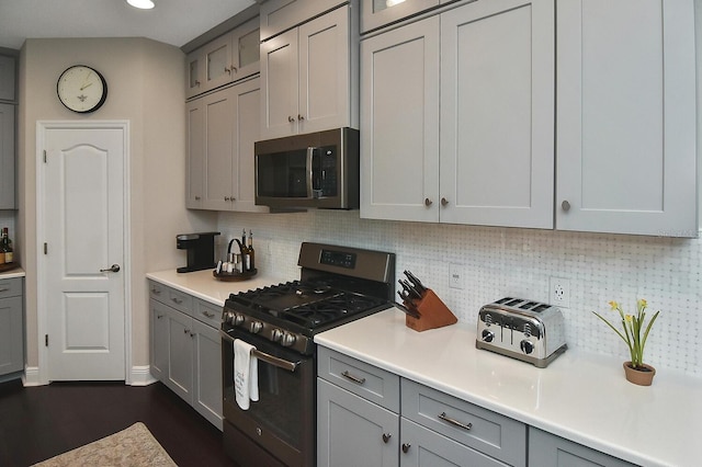 kitchen with stainless steel appliances, gray cabinets, dark hardwood / wood-style flooring, and tasteful backsplash