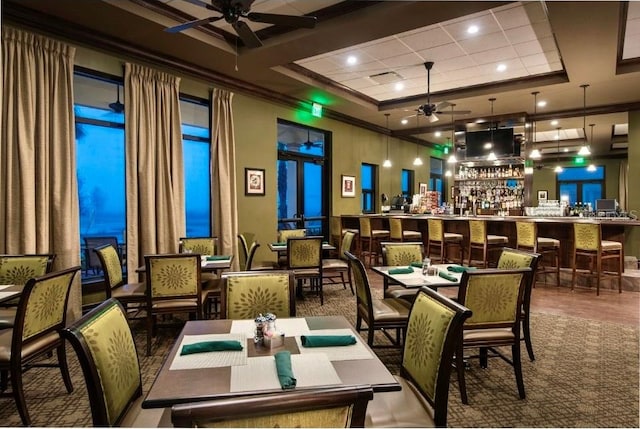 dining space featuring a towering ceiling, ornamental molding, ceiling fan, wood finished floors, and wet bar