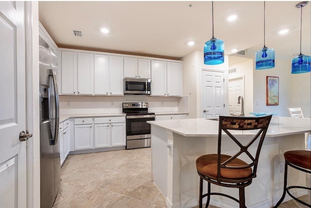 kitchen with a center island with sink, white cabinets, appliances with stainless steel finishes, a kitchen breakfast bar, and hanging light fixtures