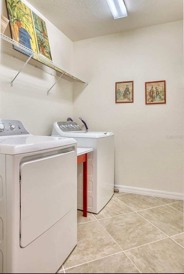 laundry room with light tile patterned floors, washing machine and dryer, a textured ceiling, laundry area, and baseboards