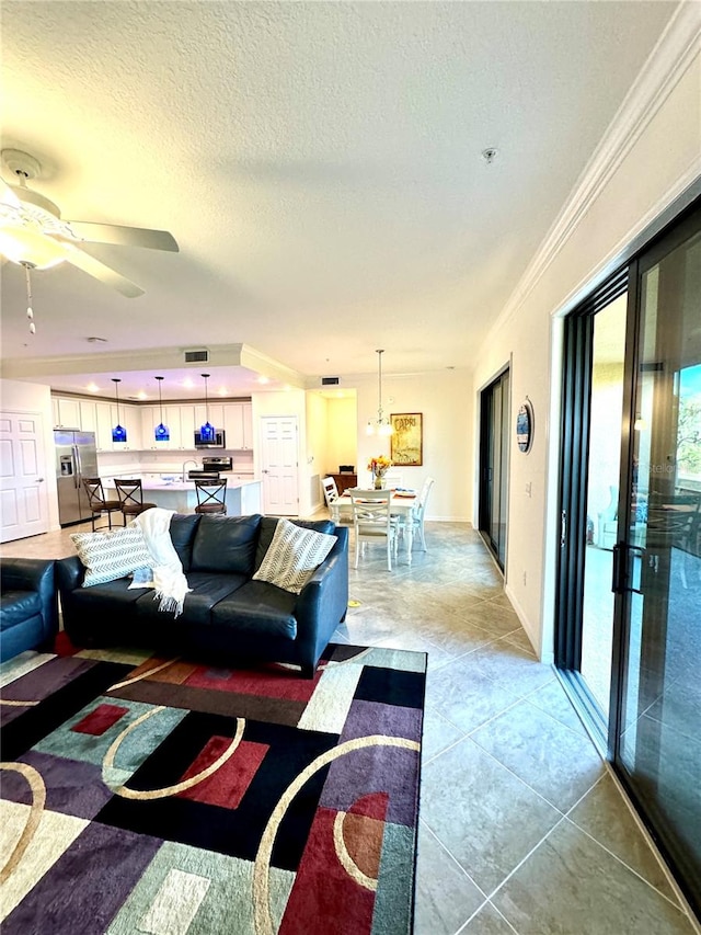 living area featuring light tile patterned floors, visible vents, a ceiling fan, crown molding, and a textured ceiling