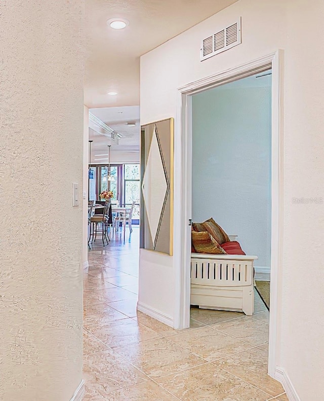 corridor with visible vents, a textured wall, and baseboards