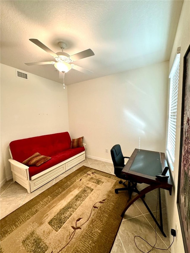 tiled office space featuring a textured ceiling, ceiling fan, visible vents, and baseboards