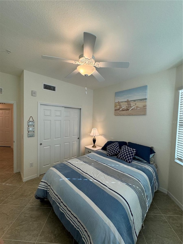 bedroom featuring visible vents, ceiling fan, a textured ceiling, dark tile patterned floors, and a closet