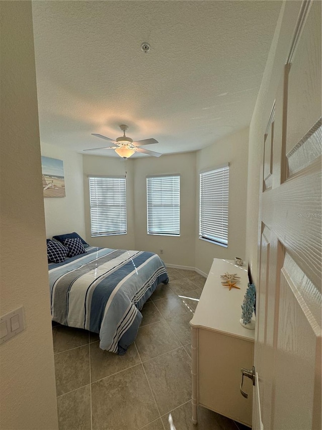 bedroom with light tile patterned floors, ceiling fan, baseboards, and a textured ceiling