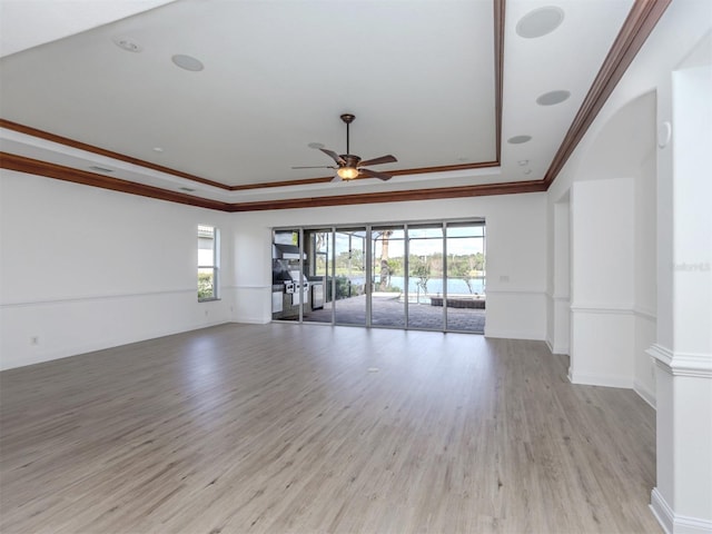 unfurnished living room with ceiling fan, a healthy amount of sunlight, a tray ceiling, and light hardwood / wood-style flooring