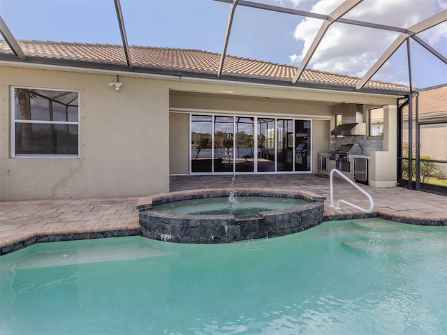 view of swimming pool featuring an in ground hot tub, an outdoor kitchen, glass enclosure, grilling area, and a patio