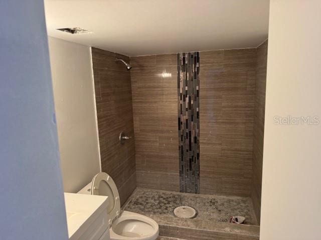 bathroom with vanity, toilet, and tiled shower