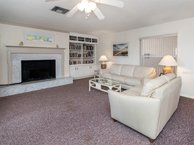 living room with carpet flooring, built in shelves, ceiling fan, and a high end fireplace