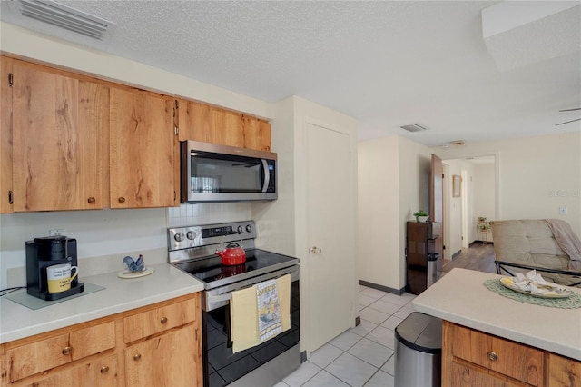 kitchen with a textured ceiling, stainless steel appliances, and light tile patterned flooring