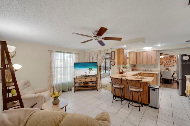 kitchen featuring ceiling fan, kitchen peninsula, stainless steel fridge, a breakfast bar area, and light tile patterned floors