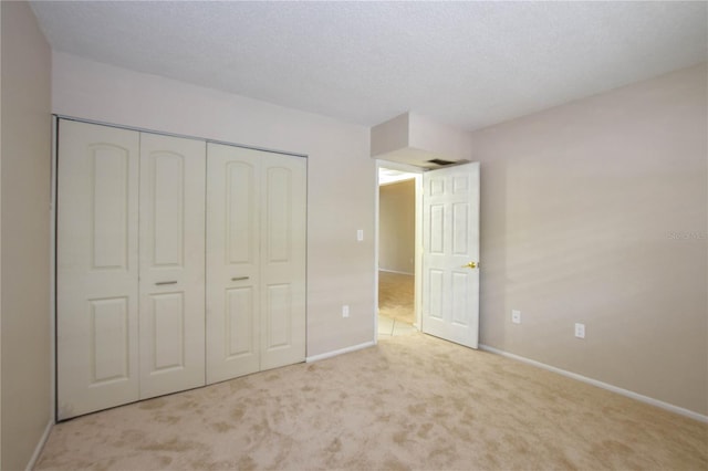 unfurnished bedroom featuring a textured ceiling, light colored carpet, and a closet