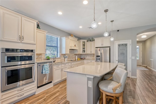 kitchen with a kitchen bar, stainless steel appliances, a center island, light hardwood / wood-style floors, and hanging light fixtures