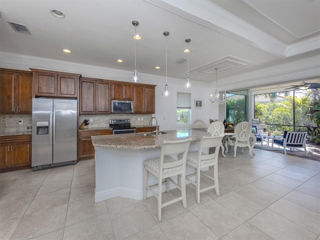 kitchen featuring pendant lighting, a kitchen island with sink, light stone countertops, tasteful backsplash, and stainless steel appliances