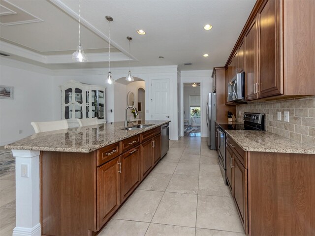 kitchen with appliances with stainless steel finishes, tasteful backsplash, a kitchen island with sink, sink, and decorative light fixtures