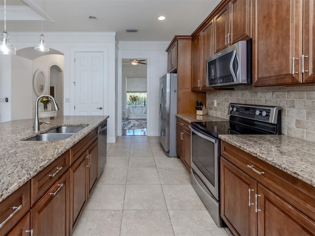 kitchen with appliances with stainless steel finishes, decorative light fixtures, light stone counters, and sink