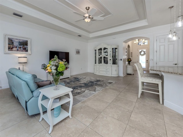 living room featuring a raised ceiling, light tile patterned flooring, ceiling fan with notable chandelier, and ornamental molding