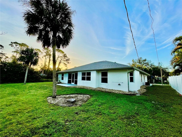 back house at dusk with a patio area and a lawn