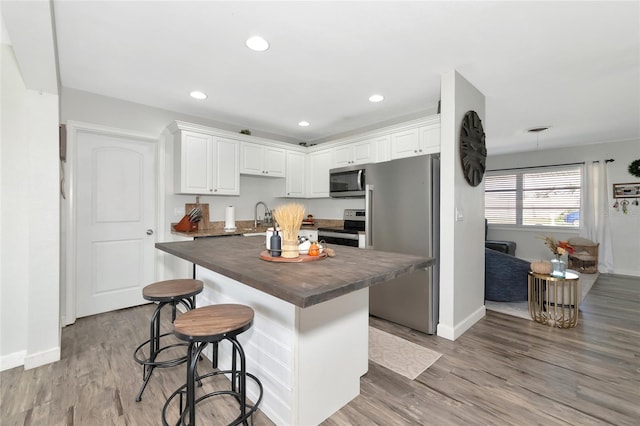 kitchen featuring light hardwood / wood-style floors, a breakfast bar area, white cabinetry, and appliances with stainless steel finishes