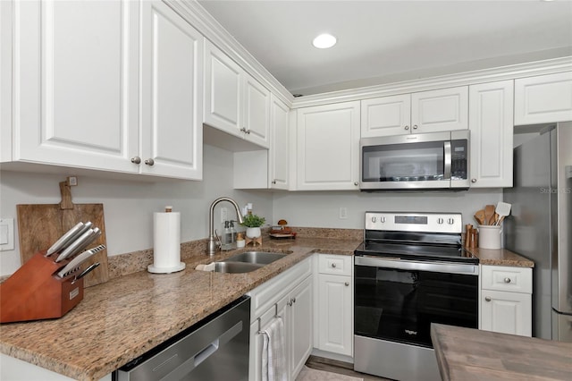 kitchen featuring stainless steel appliances, light stone countertops, white cabinetry, and sink