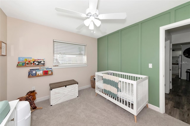 bedroom featuring a crib, ceiling fan, and light carpet