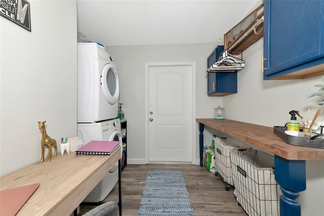 washroom featuring dark wood-type flooring, stacked washing maching and dryer, and cabinets