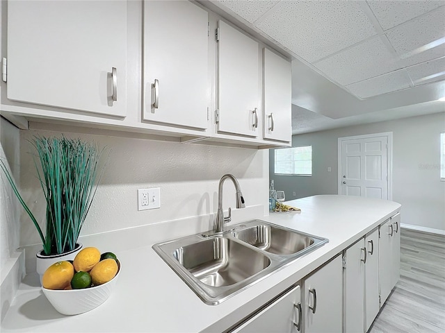 kitchen with white cabinets, a paneled ceiling, light hardwood / wood-style flooring, and sink