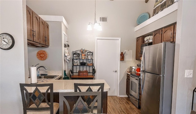 kitchen with sink, decorative light fixtures, light hardwood / wood-style floors, kitchen peninsula, and stainless steel appliances