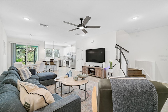 living room with light hardwood / wood-style floors and ceiling fan with notable chandelier