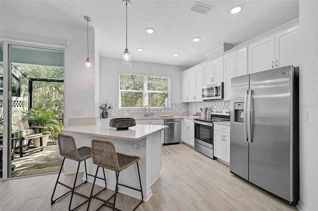 kitchen featuring light wood-type flooring, appliances with stainless steel finishes, white cabinets, a breakfast bar area, and kitchen peninsula