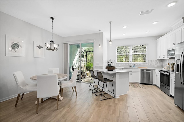 kitchen featuring light wood-type flooring, appliances with stainless steel finishes, pendant lighting, white cabinets, and a center island