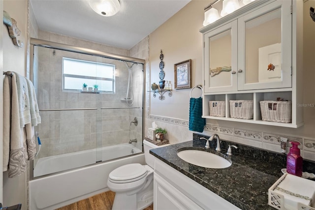 full bathroom featuring toilet, hardwood / wood-style floors, bath / shower combo with glass door, tile walls, and vanity