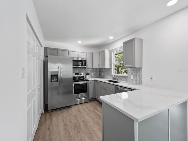 kitchen with stainless steel appliances, light hardwood / wood-style floors, kitchen peninsula, and gray cabinets