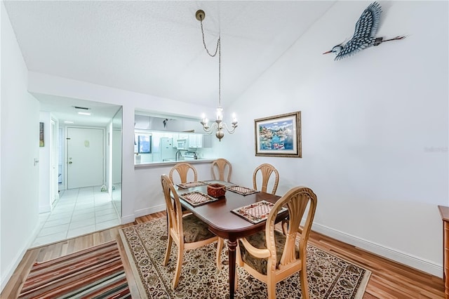 dining room featuring a chandelier, a textured ceiling, light hardwood / wood-style floors, and lofted ceiling