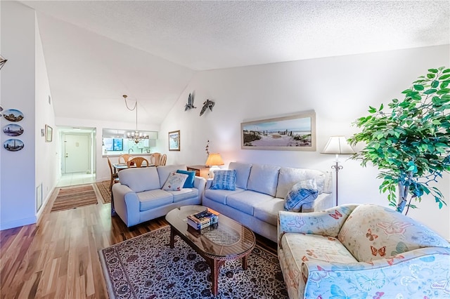 living room featuring hardwood / wood-style floors, lofted ceiling, a textured ceiling, and an inviting chandelier