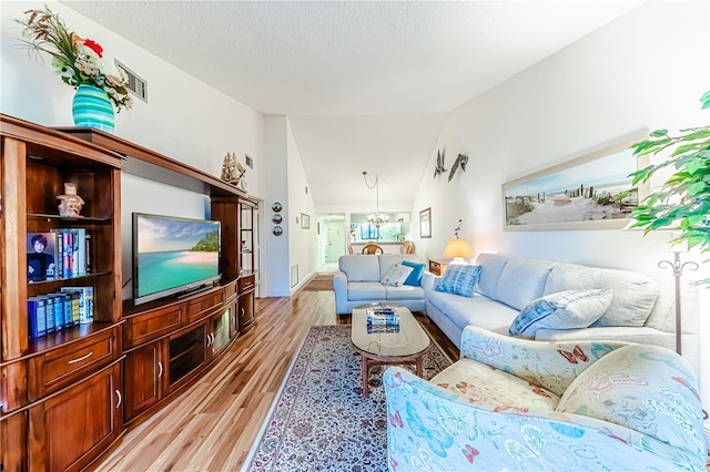 living room featuring light hardwood / wood-style floors, an inviting chandelier, a textured ceiling, and vaulted ceiling