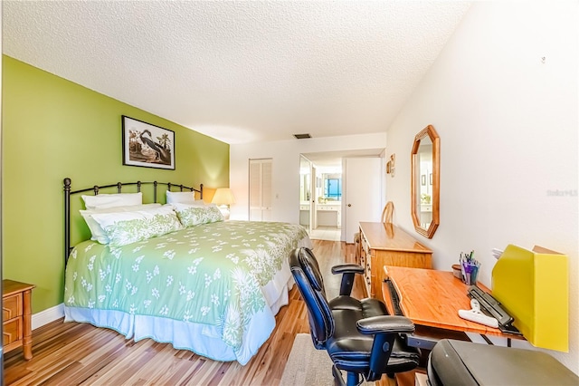 bedroom with ensuite bath, a closet, a textured ceiling, and light wood-type flooring