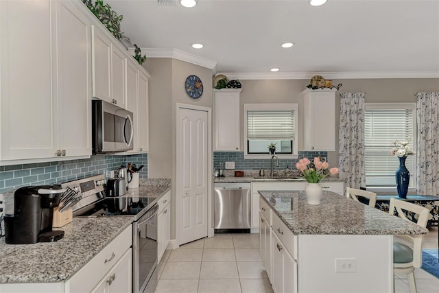 kitchen with light stone countertops, appliances with stainless steel finishes, ornamental molding, a kitchen island, and white cabinetry