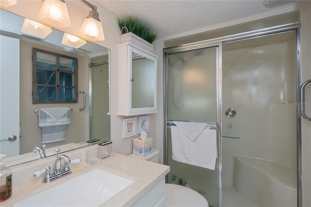 bathroom featuring vanity, toilet, a shower with shower door, and a textured ceiling