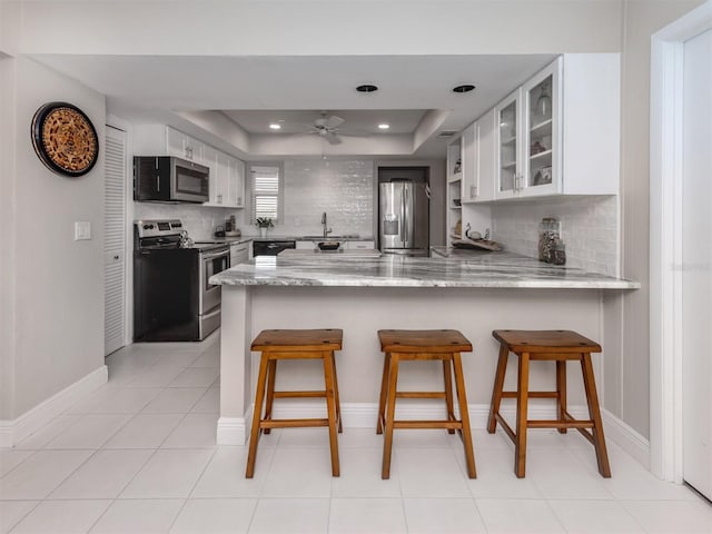 kitchen with kitchen peninsula, appliances with stainless steel finishes, a kitchen bar, a tray ceiling, and white cabinets