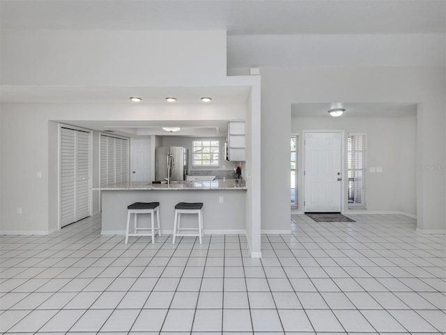 kitchen with stainless steel fridge, light tile patterned floors, white cabinetry, a kitchen bar, and kitchen peninsula